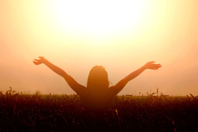 girl lifting her hands to the sun setting sky